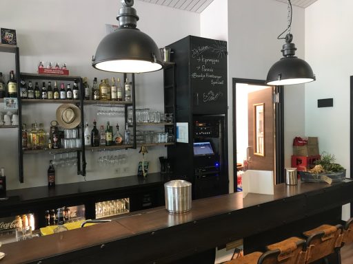 Modern bar with bottles, a cash register, and pendant lights, featuring a warm, inviting ambiance.